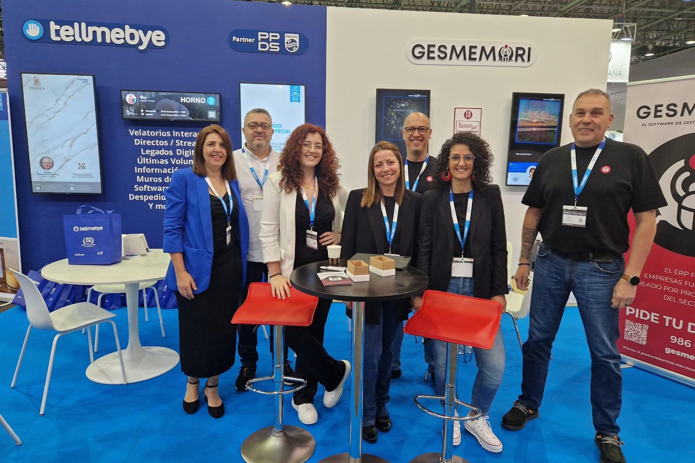 Estand compartido de Tellmebye y Gesmemori en Funergal 2024: los dos equipos posan juntos bajo los rótulos de ambas marcas, con las pantallas de velatorios interactivos detrás.